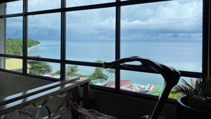 A room with a large window overlooking a beach and ocean, with a wooden bench and a potted plant inside. - Aqua Frontier Hotel and Restaurant (Lobo)