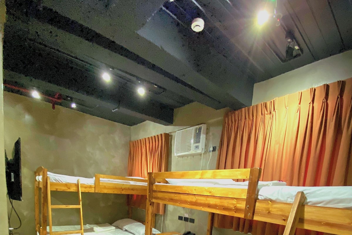 A dormitory room with bunk beds, a desk, and a ceiling fan.
