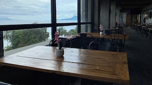 A restaurant with large windows offering a view of the sea and mountains. Tables are arranged with chairs, and there is a potted plant on one table. - Aqua Frontier Hotel and Restaurant (Lobo)