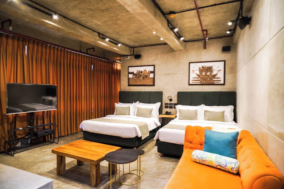 A hotel room with two beds, a sofa, a TV, and a wooden table.