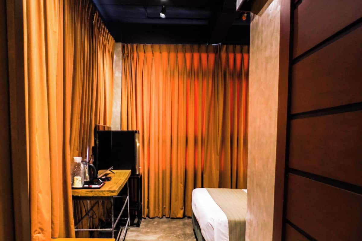 A narrow hotel room with a bed, a desk, and a television.
