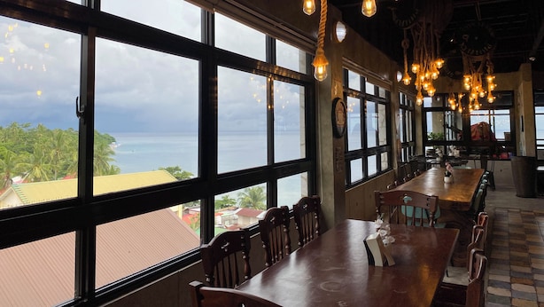 A restaurant with large windows, wooden tables, and hanging light fixtures. - Aqua Frontier Hotel and Restaurant (Lobo)