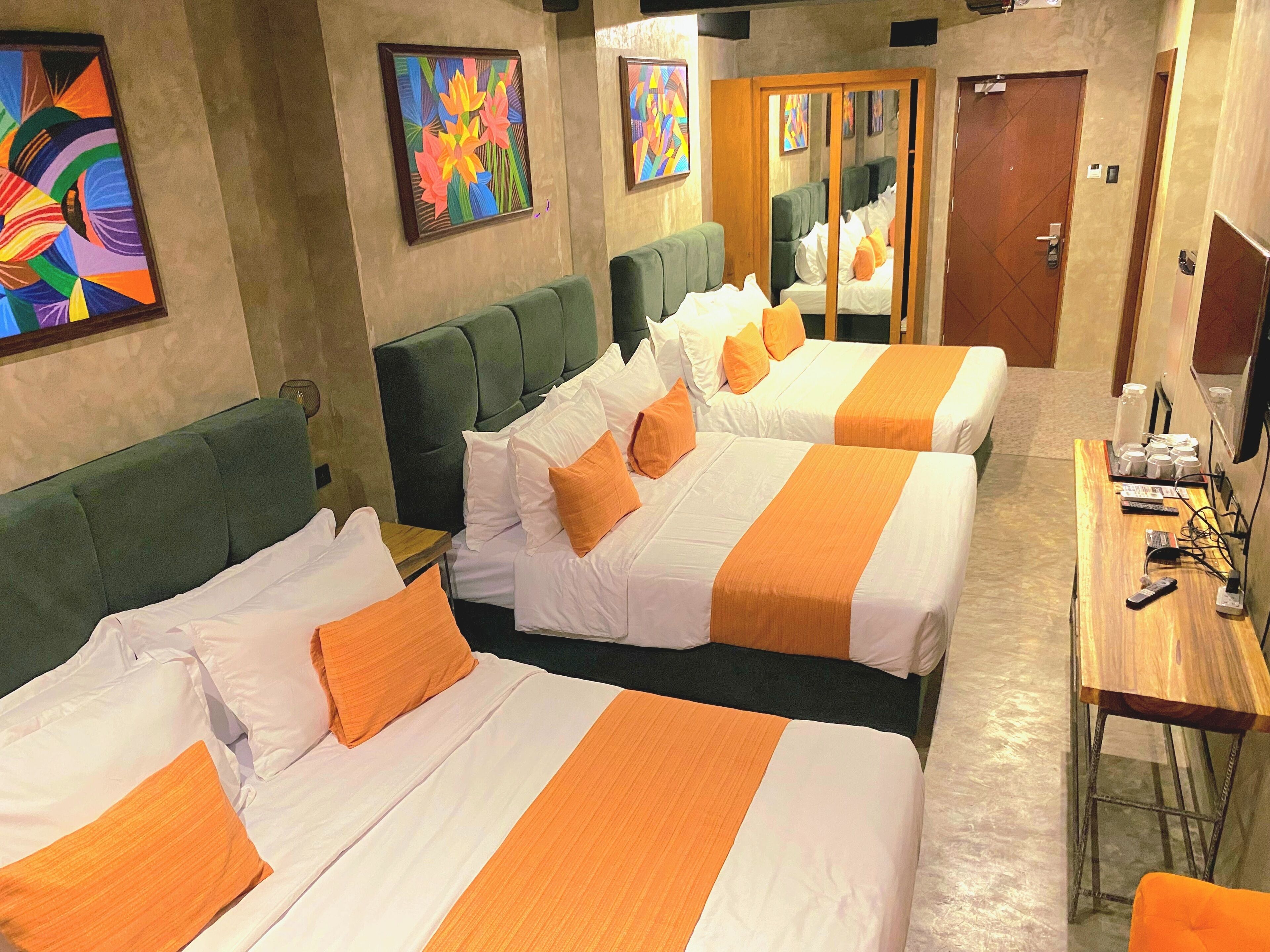 Een hotelkamer met twee bedden, elk met wit en oranje beddengoed, een houten nachtkastje en een bureau met stoel.