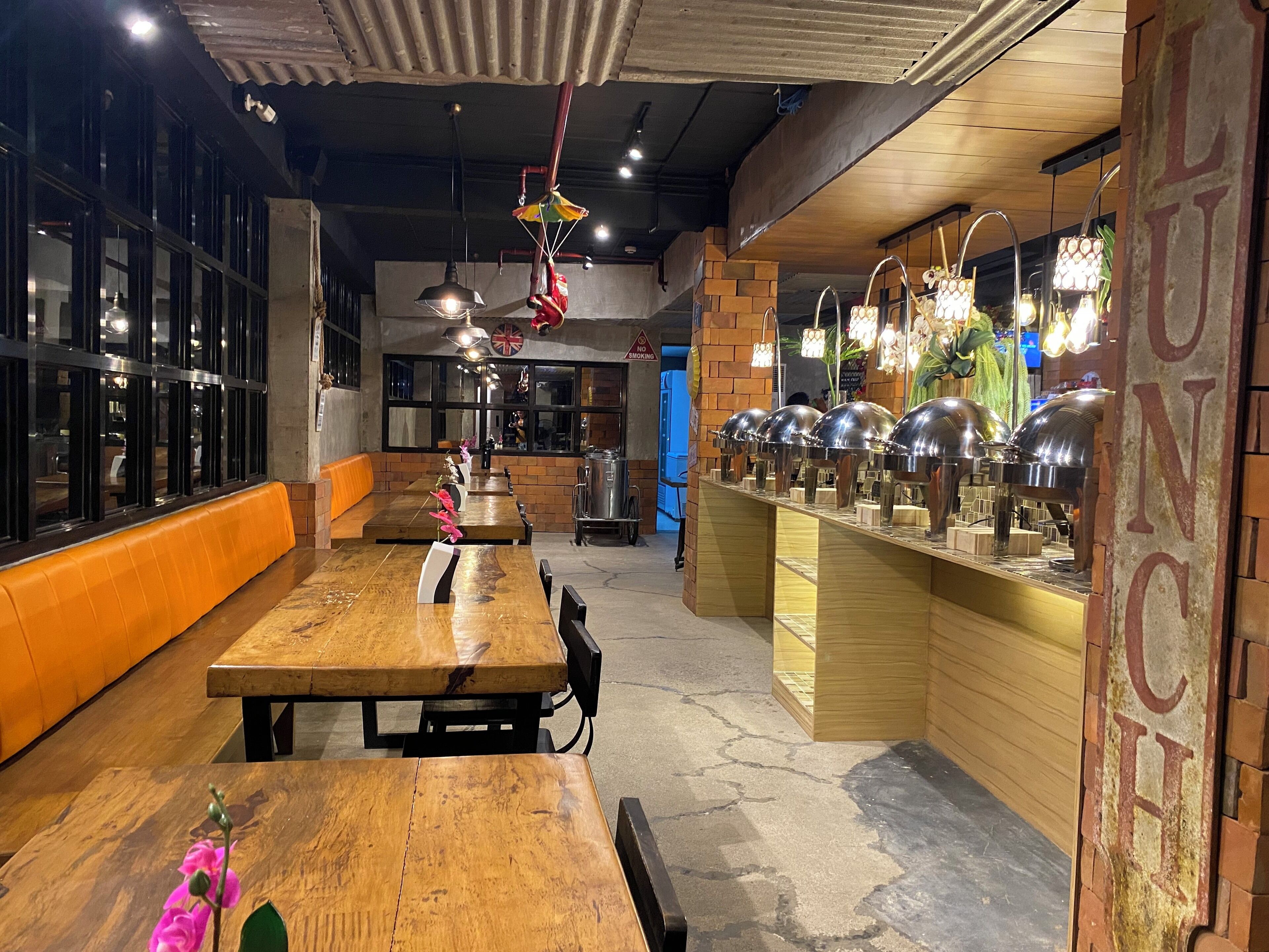 A restaurant with long wooden tables, a buffet area, and brick walls.
