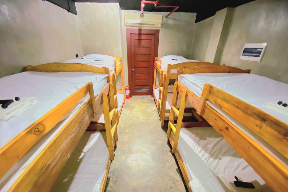 A corridor with four wooden bunk beds aligned on either side, leading to a door at the end.