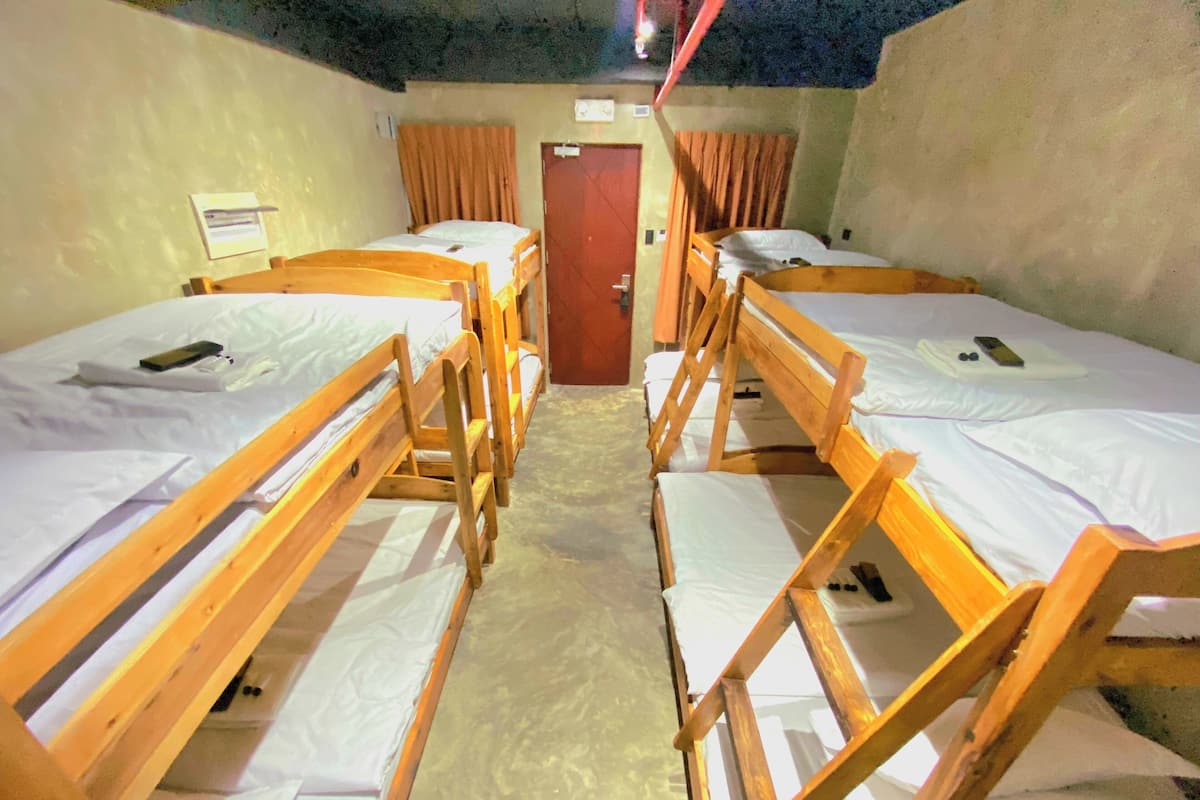 A room with four wooden bunk beds arranged in a row, a door, and a light fixture on the ceiling.
