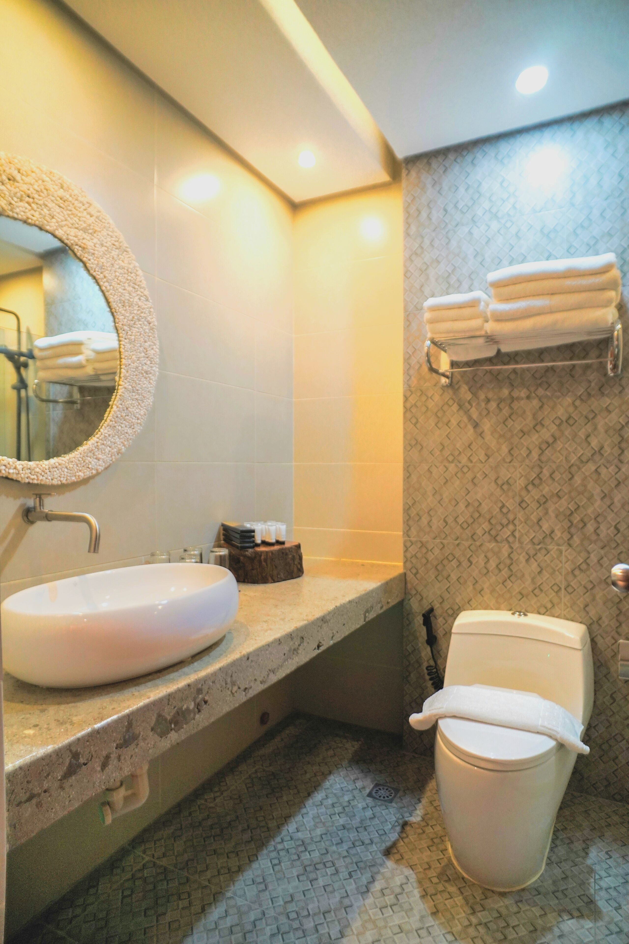 A bathroom with a round mirror, a sink, a toilet, and a towel rack.