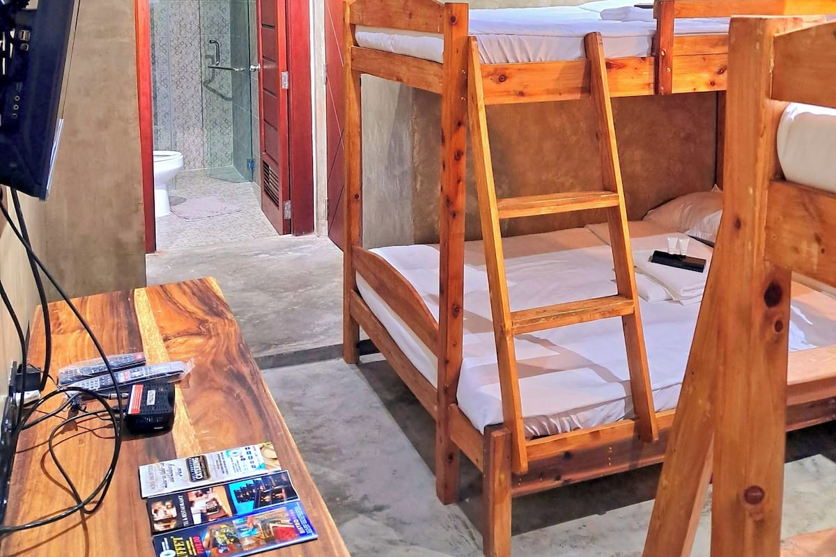 A room with bunk beds, a wooden desk with a computer and magazines, and a bathroom visible through an open door.