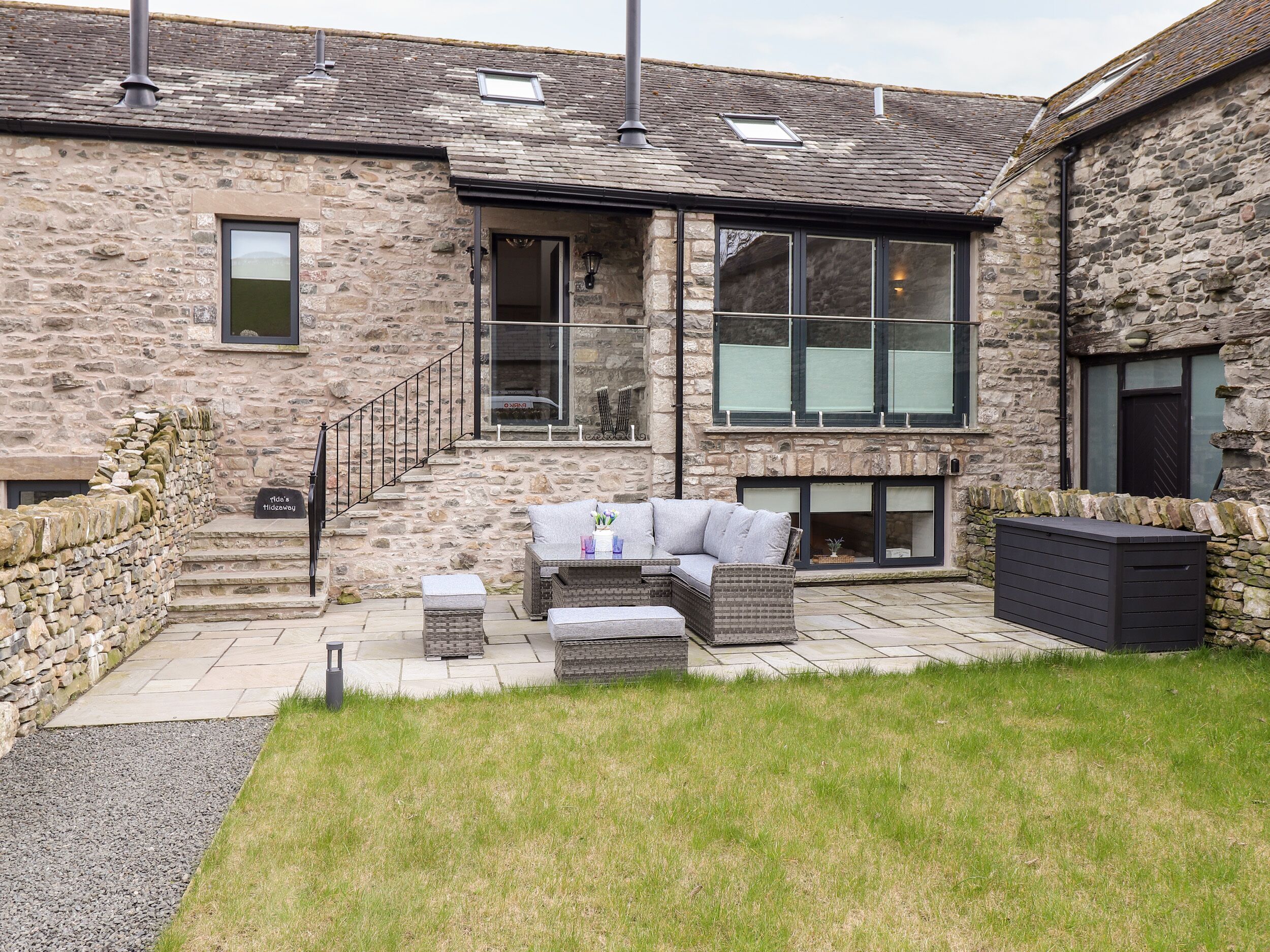 A stone building with a modern outdoor seating area, a staircase, and a grassy lawn.