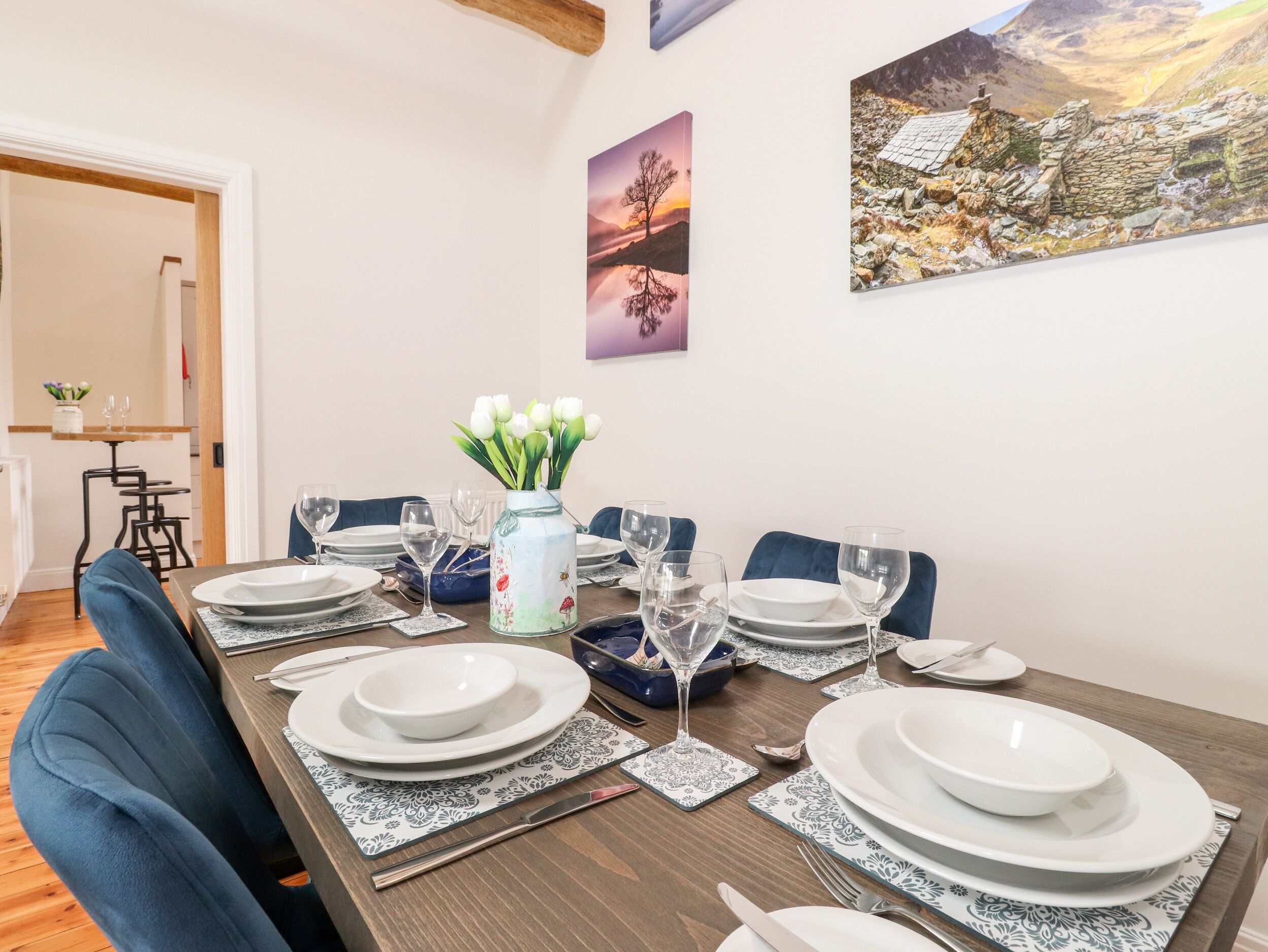 A dining area with a wooden table set for four, white plates, and a vase with white flowers.
