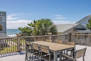 An outdoor patio with a table and chairs, a wooden deck, and a view of the ocean.
