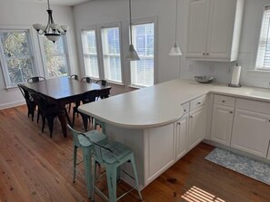 A modern kitchen with a central island, wooden dining table, and bar stools.