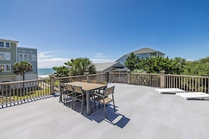 A deck with a table and chairs, overlooking a beach and ocean.