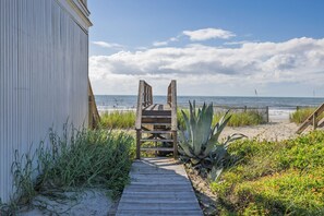 A wooden pathway leading to a beach chair, with a building on the left and a fence on the right.