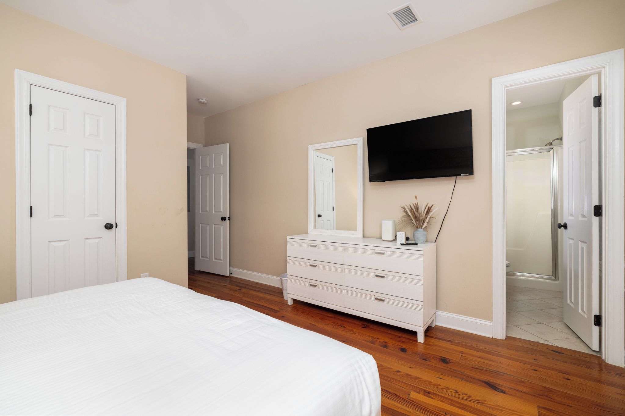 A bedroom with a bed, dresser, TV, and a door leading to a bathroom.