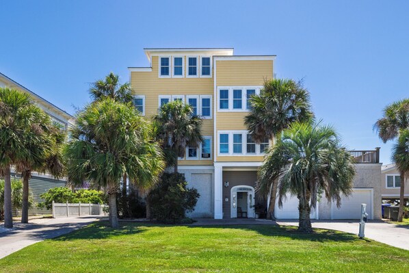 A multi-story residential building with a front entrance, surrounded by palm trees and a well-maintained lawn.