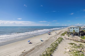 A beach with a building on the right, a sandy shore, and the ocean. - Spacious 5-Bedroom Beach House with Stunning Views & Rooftop Deck (Folly Beach)