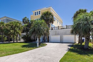 A residential building with a two-story structure, a covered driveway, and palm trees.