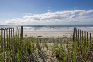 A beach with a wooden fence and tall grass in the foreground, leading to the ocean.