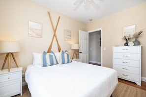 A bedroom with a large bed, white nightstands, a dresser, and artwork on the walls. - Spacious 5-Bedroom Beach House with Stunning Views & Rooftop Deck (Folly Beach)