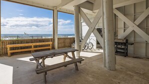 Un área de estar al aire libre con un banco de madera y una mesa de picnic, con vista a una playa que tiene una valla de madera y una bicicleta.