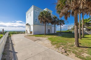 A two-story building with a white exterior, a covered porch, and a clear view of the ocean.