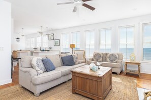A spacious living room with a large sofa, a coffee table, and a dining area with a kitchen in the background. - Stunning 4-Bedroom Oceanfront Home with Rooftop Deck and 360-Degree Views (Folly Beach)