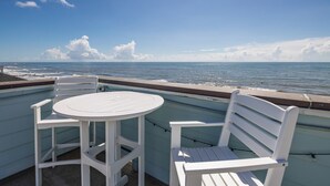 Una mesa blanca y dos sillas blancas en un balcón con vista al océano.