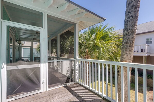 Een overdekt terras met een witte balustrade, uitzicht op een huis en een palmboom.