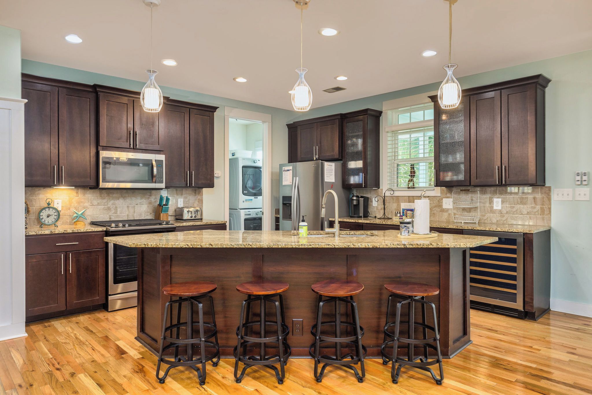 A modern kitchen with dark wood cabinets, stainless steel appliances, a granite countertop, and bar stools.