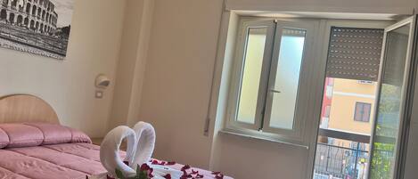 A hotel room with a bed, a window with blinds, and a view of the outside.