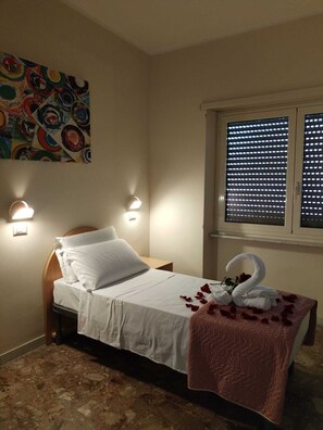 A single bed with white linens, a pink throw blanket, and a swan-shaped towel arrangement. There are two wall-mounted lights and a colorful abstract painting above the bed. - Palazzo Sant'Antonio Roma (Rome)