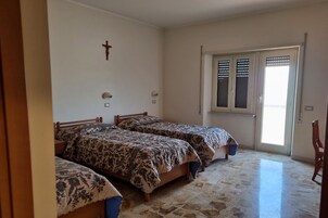 Egy szoba, amelyben két ágy, egy feszület a falon, redőnyös ablak és egy ajtó található.