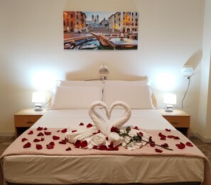 A hotel room with a bed, two bedside lamps, a painting of a cityscape, and rose petals arranged on the bed. - Palazzo Sant'Antonio Roma (Rome)