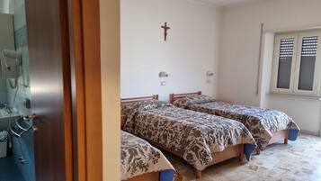 Una camera da letto con due letti, una croce appesa al muro e una finestra con persiane.