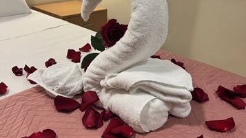 A bed with a swan-shaped towel arrangement, rose petals, and a single rose.