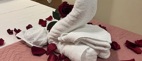A bed with a swan-shaped towel arrangement, rose petals, and a single rose.
