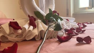 En seng med pink sengetøj, et hjerteformet håndklæde og rosenblade.