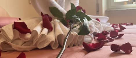 A bed with pink bedding, a heart-shaped towel, and rose petals.