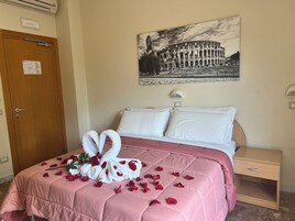 Een hotelkamer met een bed, een nachtkastje, een wandlamp en een deur met een bordje.