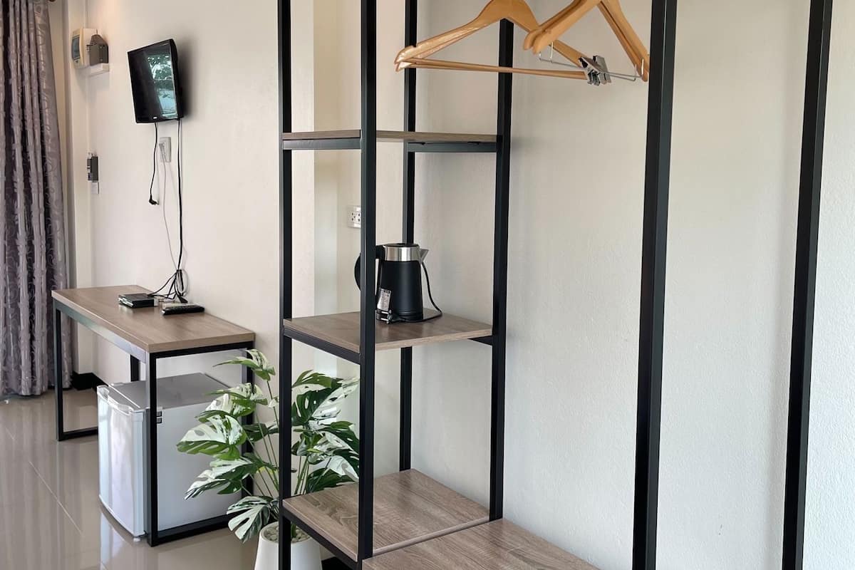 A modern hotel room with a wooden desk, a coffee maker, a TV, and a plant.