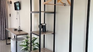 Una habitación de hotel moderna con un escritorio de madera, una cafetera negra, un televisor montado en la pared y una planta en maceta.