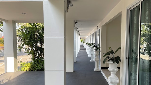 Un pasillo cubierto con columnas blancas y plantas en macetas, que conduce a un edificio con grandes ventanales.