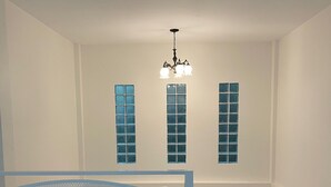 Una habitación con un banco blanco, una araña y tres ventanas con vidrios azules.