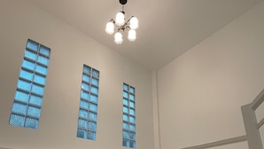 Una escalera con barandillas blancas y peldaños estampados, que conduce a un rellano con tres ventanas de vidrio azulado.
