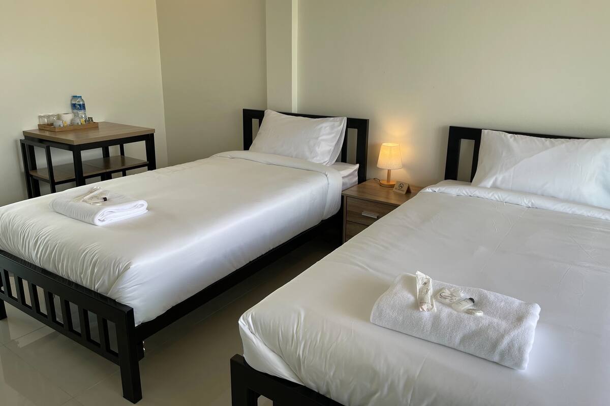 A hotel room with two single beds, a small wooden table with a water dispenser, and a nightstand with a lamp.