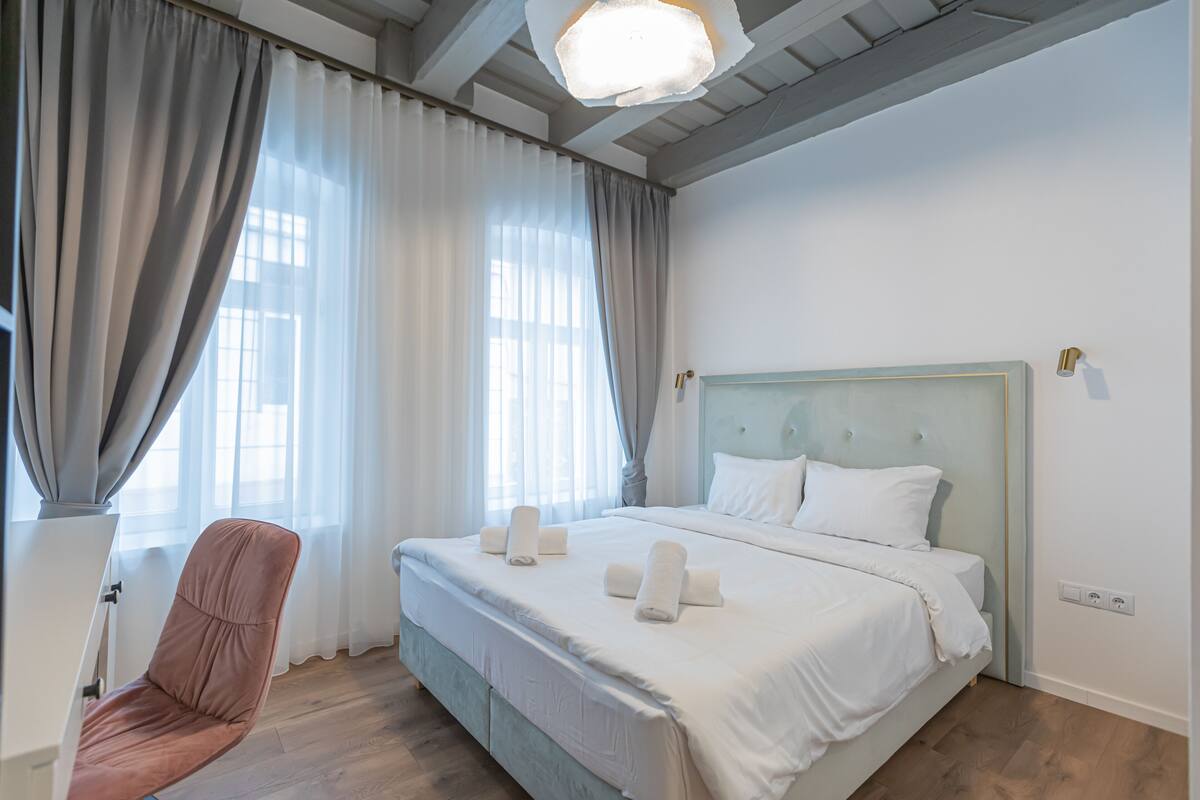 Ein Schlafzimmer mit einem Bett, einem Sessel und einem großen Fenster mit Vorhängen.