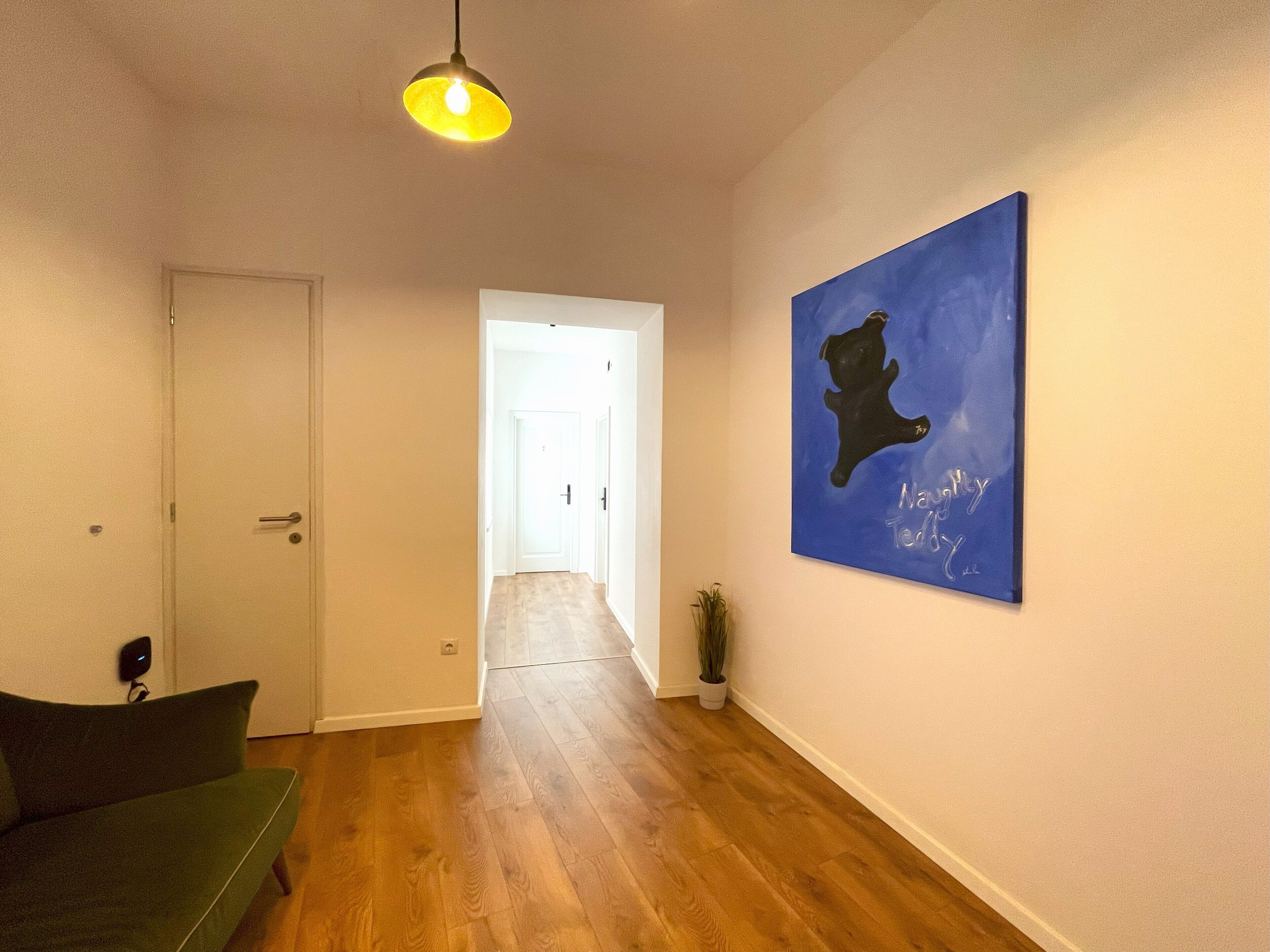A hallway with wooden flooring, a green sofa, a white door, and a blue painting on the wall.