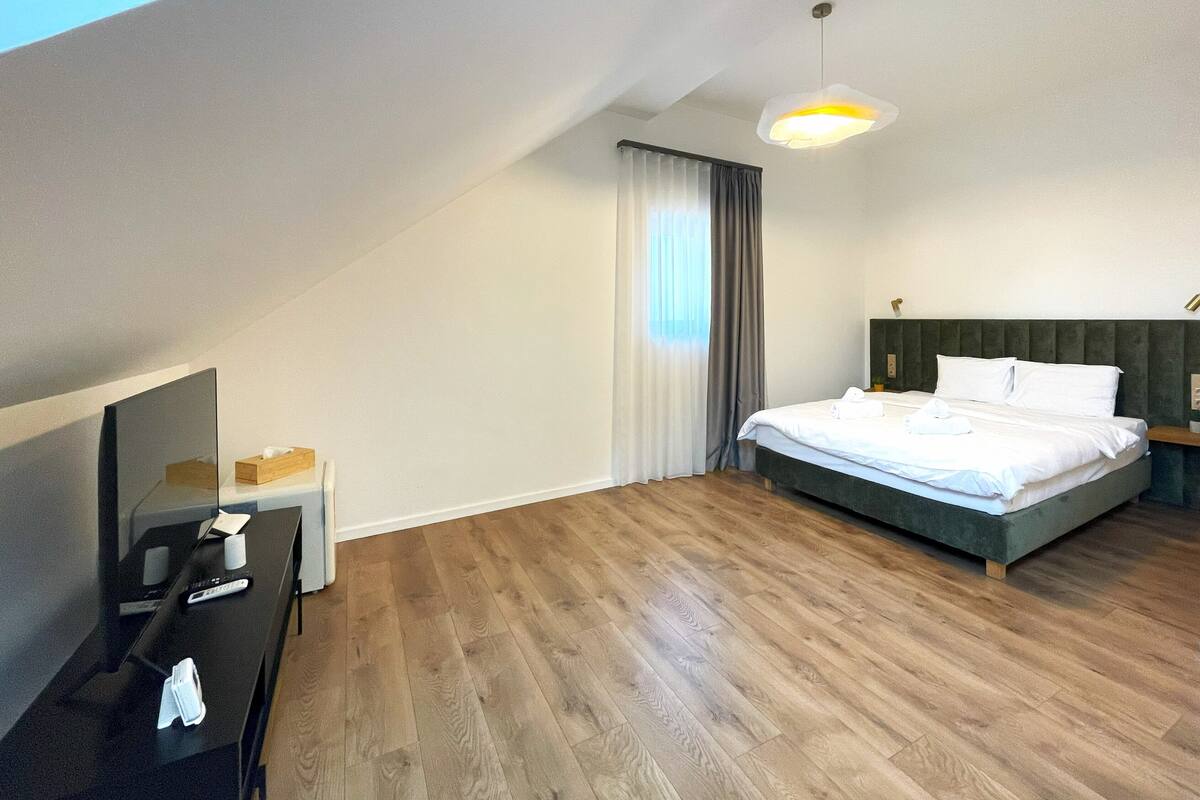 Ein modernes Hotelzimmer mit einem großen Bett, einem Schreibtisch mit Spiegel und einem Fenster mit Vorhängen.