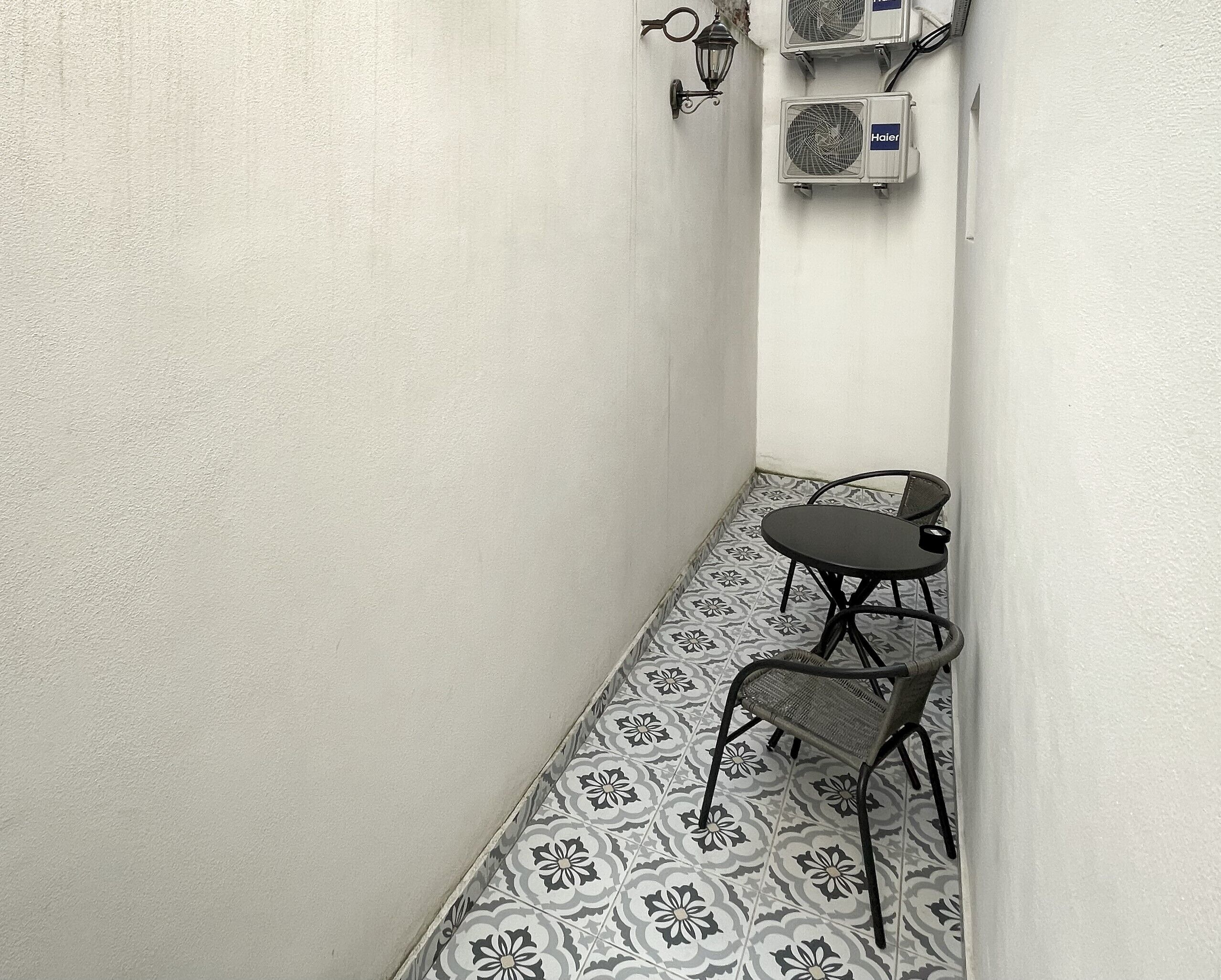 A narrow hallway with patterned floor tiles, a small table with two chairs, and two wall-mounted air conditioning units.
